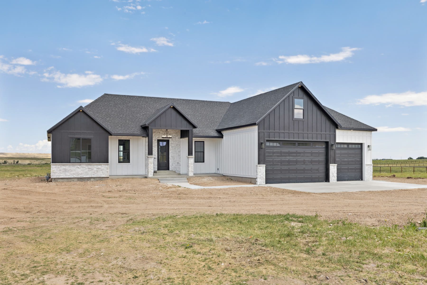 Black-and-white modern farmhouse exterior with stone accents and a three-car garage under a Wyoming sky