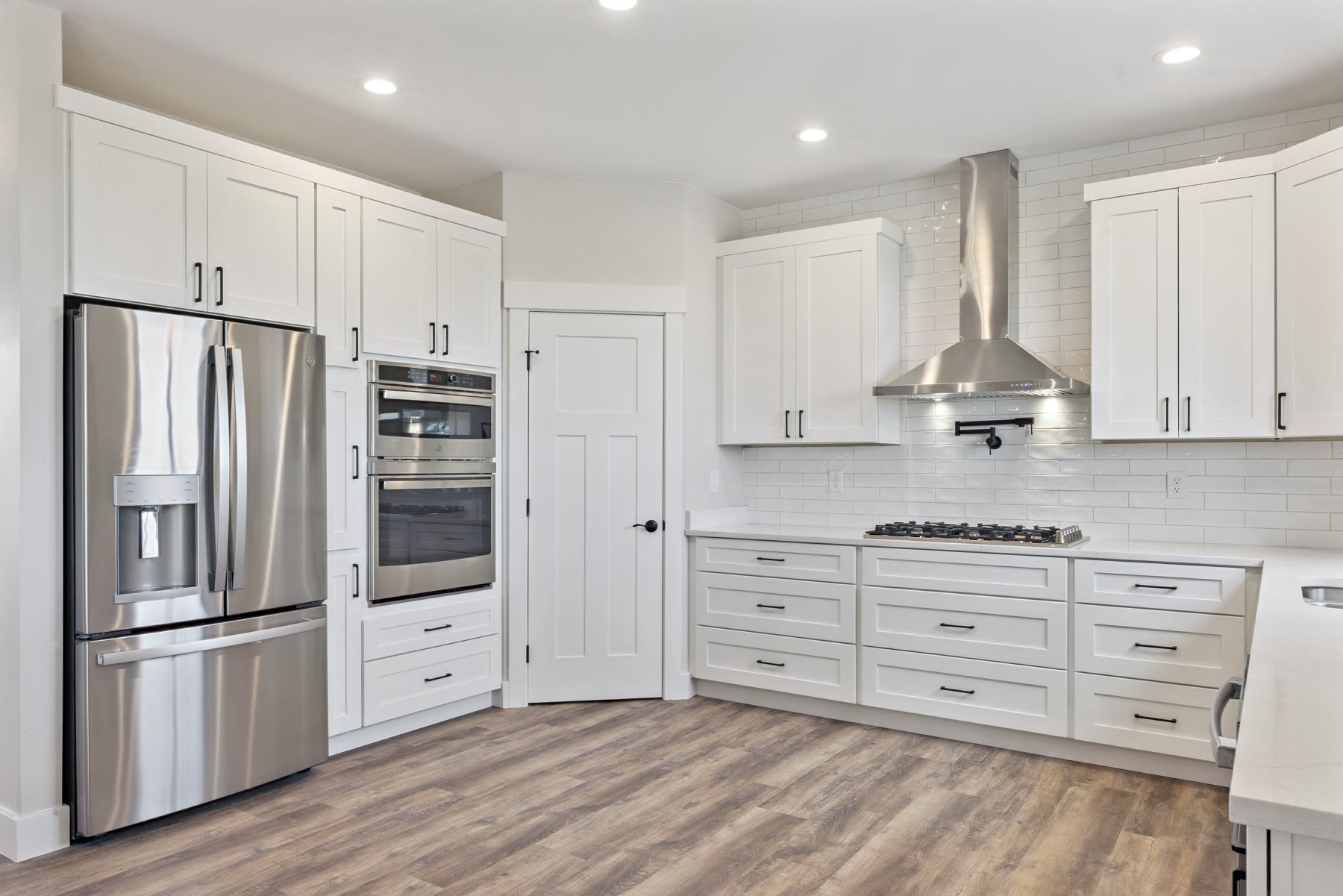 Kitchen with white shaker cabinets, stainless appliances, pot filler, and wood-look flooring