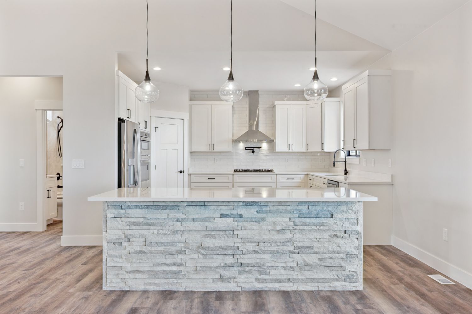 Open kitchen with a stacked-stone island, white shaker cabinets, and glass pendants in a JR Prime home