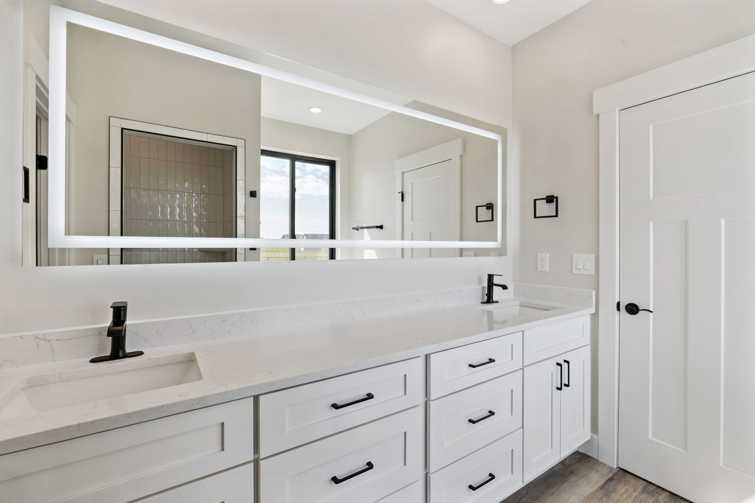 Bathroom double vanity with white shaker cabinets, black fixtures, and LED mirror